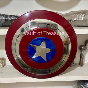 May include: A Captain America shield with a red outer ring, a silver inner ring, and a blue and silver star in the center. The text "Vault of Treasure" is visible on the shield. The shield is a circular shape.