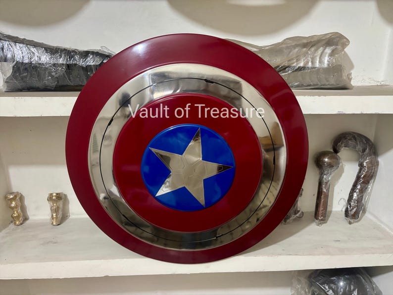 May include: A Captain America shield with a red outer ring, a silver inner ring, and a blue and silver star in the center. The text "Vault of Treasure" is visible on the shield. The shield is a circular shape.