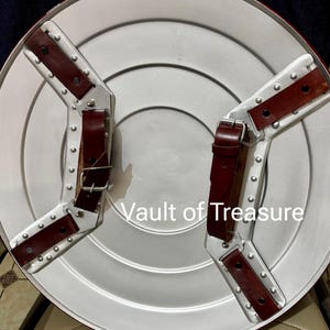 May include: A silver-colored shield with a red border and two brown leather straps. The shield has a circular design with a series of concentric circles. The text "Vault of Treasure" is visible on the shield.