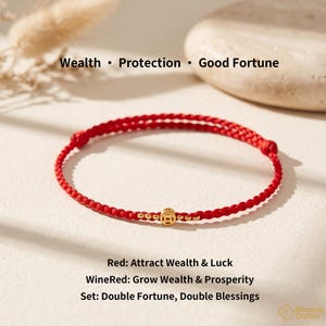 May include: A red braided cord bracelet featuring a small gold-colored circular charm with a square cutout in the center. The text Wealth • Protection • Good Fortune appears above, and Red: Attract Wealth & Luck, WineRed: Grow Wealth & Prosperity, Set: Double Fortune, Double Blessings appears below.