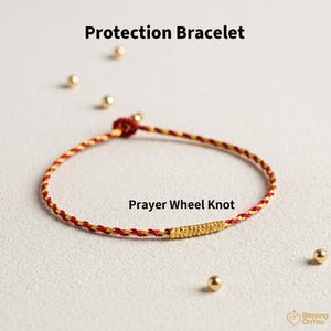 Puede incluir: Una pulsera de protección roja y dorada con un diseño de nudo de rueda de oración. La pulsera está hecha de cordón tejido y presenta un cierre dorado. Pequeñas cuentas doradas están dispersas alrededor de la pulsera.