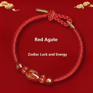 Può includere: Bracciale in agata rossa con dettagli dorati e il testo "Red Agate" e "Zodiac Luck and Energy". Il bracciale è rosso e presenta perline decorative con disegni dorati. Lo sfondo è rosso pieno.