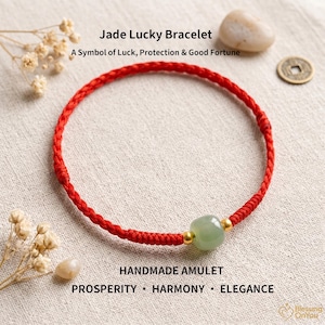 May include: A red braided cord bracelet featuring a single smooth, pale green jade bead flanked by two small gold-toned metal spheres. The text "Jade Lucky Bracelet" and "A Symbol of Luck, Protection & Good Fortune" appears above the bracelet.