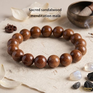 Puede incluir: Una pulsera mala de meditación de sándalo marrón con cuentas grandes y redondas. La pulsera se muestra sobre una superficie texturizada de color blanquecino, con el texto "Sacred sandalwood menditation mala" encima. Un cuenco tibetano de latón está en el fondo.