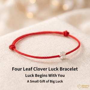 Op de afbeelding: Een rood koordarmbandje met een kleine zilverkleurige bedel in de vorm van een klavertjevier. De tekst Four Leaf Clover Luck Bracelet, Luck Begins With You en A Small Gift of Big Luck staat onder het armbandje gedrukt, inclusief een logo.