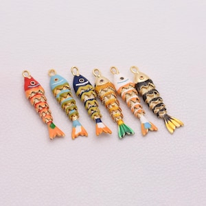Puede incluir: Seis colgantes coloridos con forma de pez y detalles metálicos dorados. Cada colgante presenta una combinación de colores única, incluyendo rojo, naranja, azul, amarillo y negro, con patrones de escamas detallados y un lazo para sujetar. Ideal para manualidades.