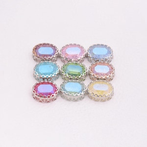 Puede incluir: Nueve gemas ovaladas iridiscentes con engastes de filigrana plateada. Las gemas muestran una gama de colores, incluyendo rosa, azul, verde y amarillo. Dispuestas en un patrón de cuadrícula sobre un fondo blanco.