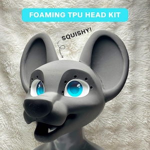 May include: A gray foaming TPU head kit featuring large rounded ears, a snout, and bright blue eyes with white surrounds. The head has small circular perforations around the eye sockets and the text FOAMING TPU HEAD KIT and SQUISHY!