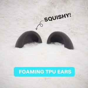 May include: Two dark gray, semi-circular, foam-like TPU ears. A black arrow points to one ear with the text SQUISHY! above it. A bright blue rectangular banner at the bottom contains the white text FOAMING TPU EARS in all capital letters.