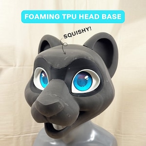 Op de afbeelding: Een donkergrijze, schuimende TPU-hoofdmal voor een fursuit, met grote, felblauwe ogen met witte randen. De tekst FOAMING TPU HEAD BASE staat bovenaan en een pijl wijst naar het voorhoofd met de tekst SQUISHY!.