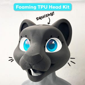 May include: A dark gray foaming TPU head kit shaped like a feline mask with large, bright blue eyes, white eye sockets, and visible texture lines. The text "Foaming TPU Head Kit" appears above, with the word "squishy!" and an arrow pointing down.