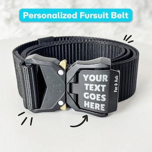 Op de afbeelding: Een zwarte nylon riem met een stevige metalen snelsluiting. De gesp is voorzien van de gegraveerde tekst "YOUR TEXT GOES HERE" en "Fur & Ash" aan de zijkant. De riem is gemaakt van duurzaam, geribbeld zwart bandmateriaal.