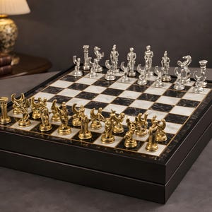 Könnte beinhalten: Schachspiel mit gold- und silberfarbenen Figuren auf einem schwarz-weiß karierten Brett. Die Schachfiguren sind in einem klassischen Stil geformt. Das Brett befindet sich in einer schwarzen Holzkiste. Eine Lampe und Bücher sind im Hintergrund.