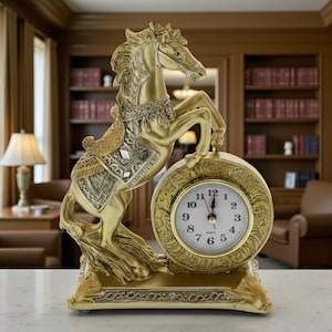 Puede incluir: Un reloj decorativo dorado con un caballo encabritado. El caballo está intrincadamente detallado con una silla de montar y una brida, y está posicionado junto a una esfera redonda con números romanos. El reloj es de cuarzo.