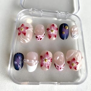 以下が含まれることがあります： 透明なプラスチックケースに入った10本のつけ爪のセット。 赤と金のアクセントのフローラルパターンや抽象的な渦巻きなど、さまざまなデザインが施されています。 ネイビーブルーまたはライトピンクのベースの爪もあります。