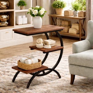 Puede incluir: Una mesa auxiliar de tres niveles con acabado en madera oscura y estructura de metal negro. La balda superior sostiene un jarrón blanco con flores blancas. La balda central exhibe objetos decorativos y la inferior una cesta tejida.