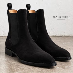 May include: A pair of black suede Chelsea boots featuring elastic side panels, a pointed toe, a low block heel, and a black pull tab at the back of each ankle. The text "BLACK SUEDE" is printed in the upper right corner of the image.