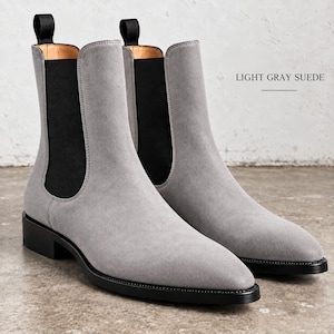 Könnte beinhalten: Ein Paar hellgraue Chelsea-Boots aus Wildleder mit schwarzen elastischen Seiteneinsätzen, schwarzen Zuglaschen an der Oberseite und schwarzen Sohlen mit niedrigem Absatz. Der Text LIGHT GRAY SUEDE ist oben rechts im Bild zu sehen.