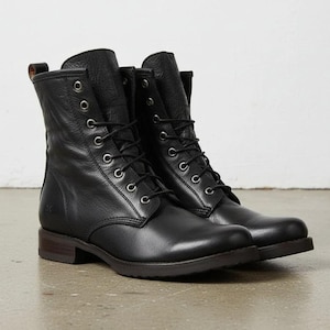 Puede incluir: Un par de botas de cuero negro con cordones, altura a media pantorrilla, punteras redondeadas y ojales metálicos plateados. Las botas tienen un tacón apilado, una parte superior de cuero texturizado y una lengüeta en la parte posterior.