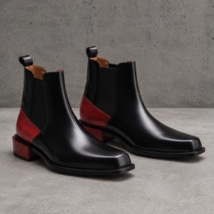 May include: A pair of black leather Chelsea boots featuring a square toe, elastic side panels, and a contrasting red leather heel and back panel. The boots include a pull tab at the top of the shaft and a low, block-shaped red heel.