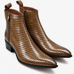 Peut inclure: Une paire de bottines marron avec un motif texturé gaufré façon crocodile. Les bottines présentent un bout pointu, un talon bloc noir et une fermeture éclair latérale ornée d'une petite breloque tête de mort. Une tirette est visible.