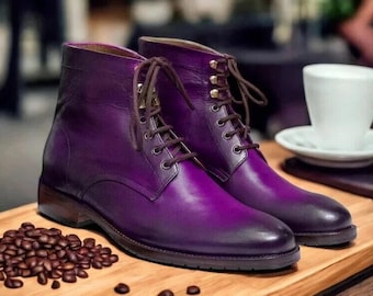 May include: A pair of deep purple leather boots with brown laces. The boots are on a wooden surface, next to coffee beans and a white cup and saucer. The boots are a stylish footwear choice.