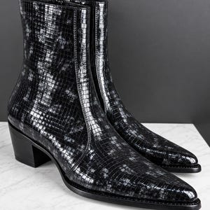May include: A pair of black ankle boots featuring a glossy, grid-like textured pattern across the surface. These boots have a pointed toe, a stacked block heel, and a side zip closure, showcasing a sleek, polished finish with subtle grey highlights.