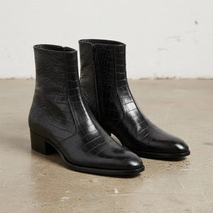 Könnte beinhalten: Ein Paar schwarze Stiefeletten mit einer strukturierten Krokodilleder-Prägung auf der gesamten Oberfläche. Die Stiefel haben eine elegante, spitz zulaufende Zehenpartie, einen seitlichen Reißverschluss und einen niedrigen Blockabsatz.