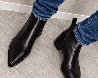 May include: A pair of black leather Chelsea boots with pointed toes, elastic side panels, and pull tabs at the heels, worn with blue denim jeans. The boots feature a smooth finish, a low block heel, and a sleek silhouette that covers the ankles.