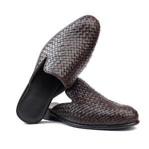 May include: Two brown leather woven slip-on shoes. The shoes have a dark brown sole and a woven pattern on the upper. The shoes are displayed on a white background.