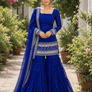 May include: A vibrant royal blue salwar kameez outfit. The ensemble includes a long-sleeved top with a square neckline and palazzo trousers. Silver embroidery details the neckline, cuffs, and trousers. A matching sheer dupatta with silver trim completes the look.