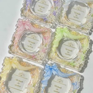 以下が含まれることがあります： パステルカラーの花柄とリボンがアクセントになった、透明アクリルフレーム6個。各フレームは正方形で、中央に円があり、「Till Death Do Us Part」の文字が入っています。リボンは紫、ピンク、緑、黄色、青の色合いです。