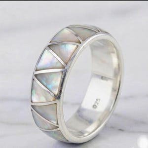 Könnte beinhalten: Ein Silberring mit einer Reihe dreieckiger Einlagen aus irisierendem weißem Perlmutt. Der Ring hat eine polierte Silberoberfläche und enthält einen deutlich sichtbaren 925er-Stempel auf der Innenseite der Metallschiene.