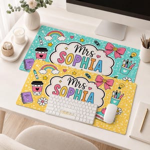 May include: Two rectangular desk mats featuring a speckled background in teal and yellow. Each mat displays a central cloud-shaped label with the text Mrs SOPHIA, surrounded by illustrations of rainbows, coffee cups, bows, and stationery items.