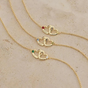 May include: Gold necklaces with intertwined heart pendants, each with a gemstone and engraved names: Evelyn, Ethan, Olivia, Chloe. The necklaces are shown on a neutral background.