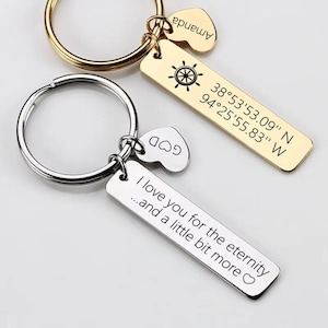 May include: Two keychains with personalized tags. One gold keychain has a tag with a ship's wheel and coordinates. The other silver keychain has a tag with the text "I love you for the eternity...and a little bit more". Both have heart-shaped charms.
