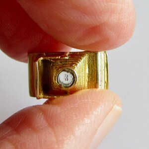 May include: A gold-colored charm in the shape of a car with a clear crystal in the center.