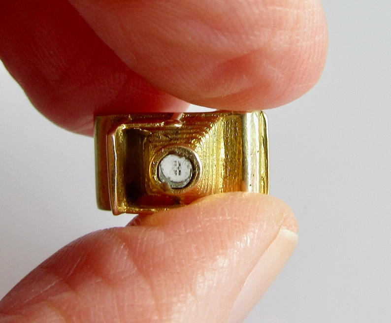 May include: A gold-colored charm in the shape of a car with a clear crystal in the center.