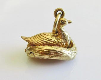 May include: A gold-colored duck charm, possibly for a necklace or bracelet. The duck is resting on a log-shaped base. The charm has a loop at the top for attachment and is highly detailed.