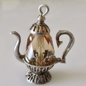 Peut inclure: Un charme de théière en argent avec un corps en verre transparent, facetté et de couleur ambre. La théière a un design détaillé et orné et une boucle pour l'accrocher.