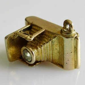 May include: A gold charm in the shape of an old-fashioned camera with a single diamond-shaped stone in the lens.