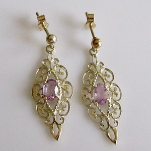 May include: A pair of gold filigree earrings with a light purple gemstone in the center of each earring.