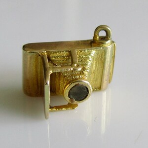 May include: A gold-toned charm in the shape of a vintage camera. The charm has a detailed design with a lens and a textured body.