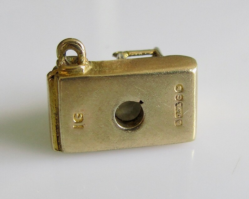 May include: Gold charm in the shape of a vintage sewing machine. The charm has a loop for attaching to a bracelet or necklace. The back of the charm is stamped with "9ct" and "1g".