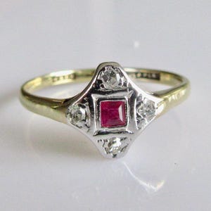 Może przedstawiać: Złoty i srebrny pierścionek z czerwonym kwadratowym kamieniem szlachetnym otoczonym czterema mniejszymi białymi kamieniami szlachetnymi.