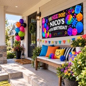 May include: A rectangular black birthday banner featuring the text YOU NEE DOH! NICO'S 6TH BIRTHDAY LET'S PARTY! surrounded by colorful illustrations of sensory toys, cubes, and fruit, displayed on a house exterior with balloons and a bench.