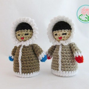 May include: Two crocheted dolls wearing brown winter coats with white trim and hats. The dolls have black hair and brown faces with red lips. One doll is wearing blue mittens and the other is wearing red mittens.