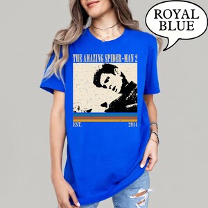 May include: Royal blue t-shirt with a graphic from "The Amazing Spider-Man 2". The design features a black and white image of a man, the text "THE AMAZING SPIDER-MAN 2", and the year "2014". The shirt is a solid royal blue colour.