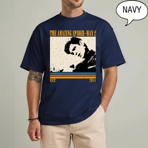 May include: Navy blue t-shirt with a vintage graphic from "The Amazing Spider-Man 2". The design includes a black and white image of a person, the film title, and the year 2014. The shirt has short sleeves and a round neck.