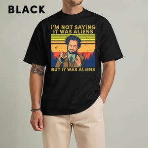 May include: Black t-shirt with the text "I'M NOT SAYING IT WAS ALIENS BUT IT WAS ALIENS" and a graphic of a man with his hands up. The text and graphic are in yellow, orange, and blue.